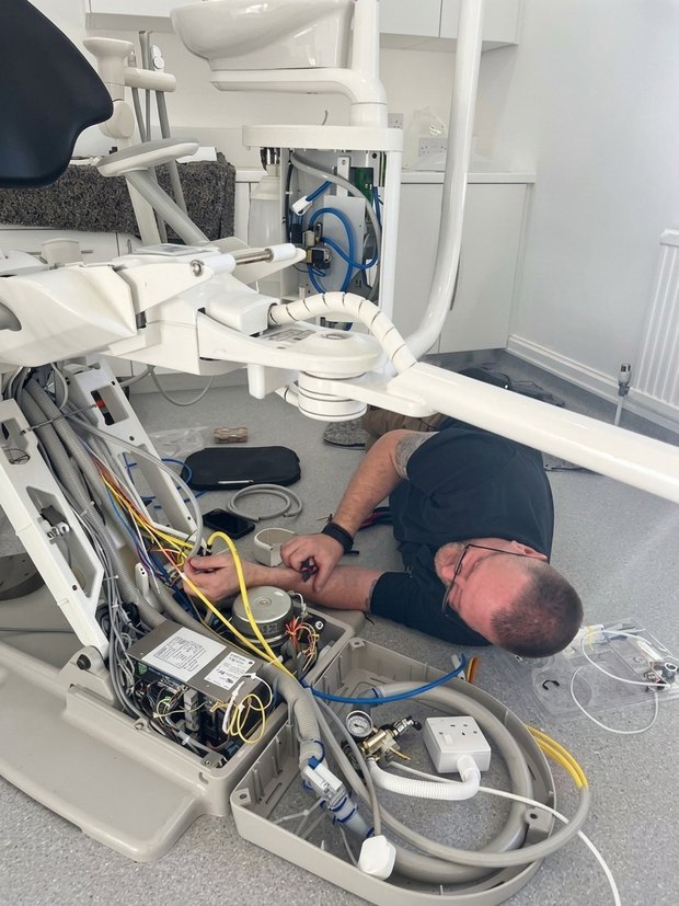 A Precision Dental engineer working on the wiring beneath a dental chair during a service visit